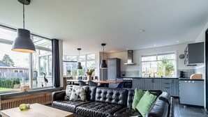 A modern living room with a leather sofa, a wooden coffee table, and a dining area with a wooden table and chairs. - Detached new 10-person Villa in Holiday Park (Kamperland)
