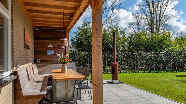 An outdoor patio with a wooden table and benches, a metal sculpture, and a well-maintained garden. - Detached new 10-person Villa in Holiday Park (Kamperland)