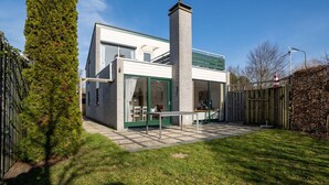 A modern two-story house with a green door, a chimney, and a patio with a table and chairs. - Holiday Home in the Middle of the Green North Sea Park Near the Beach Entrance (Ouddorp)