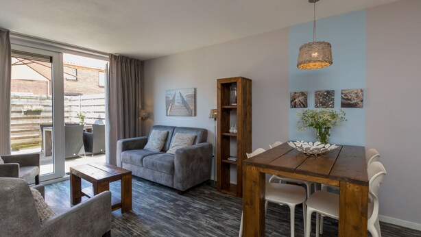 A modern living room with a grey sofa, wooden coffee table, and a dining area with a wooden table and white chairs. - Holiday Home Near the Beach Zoutelande (Zoutelande)