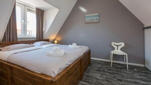 A bedroom with a wooden bed, a white chair, a painting on the wall, and a window with curtains. - Holiday Home Near the Beach Zoutelande (Zoutelande)