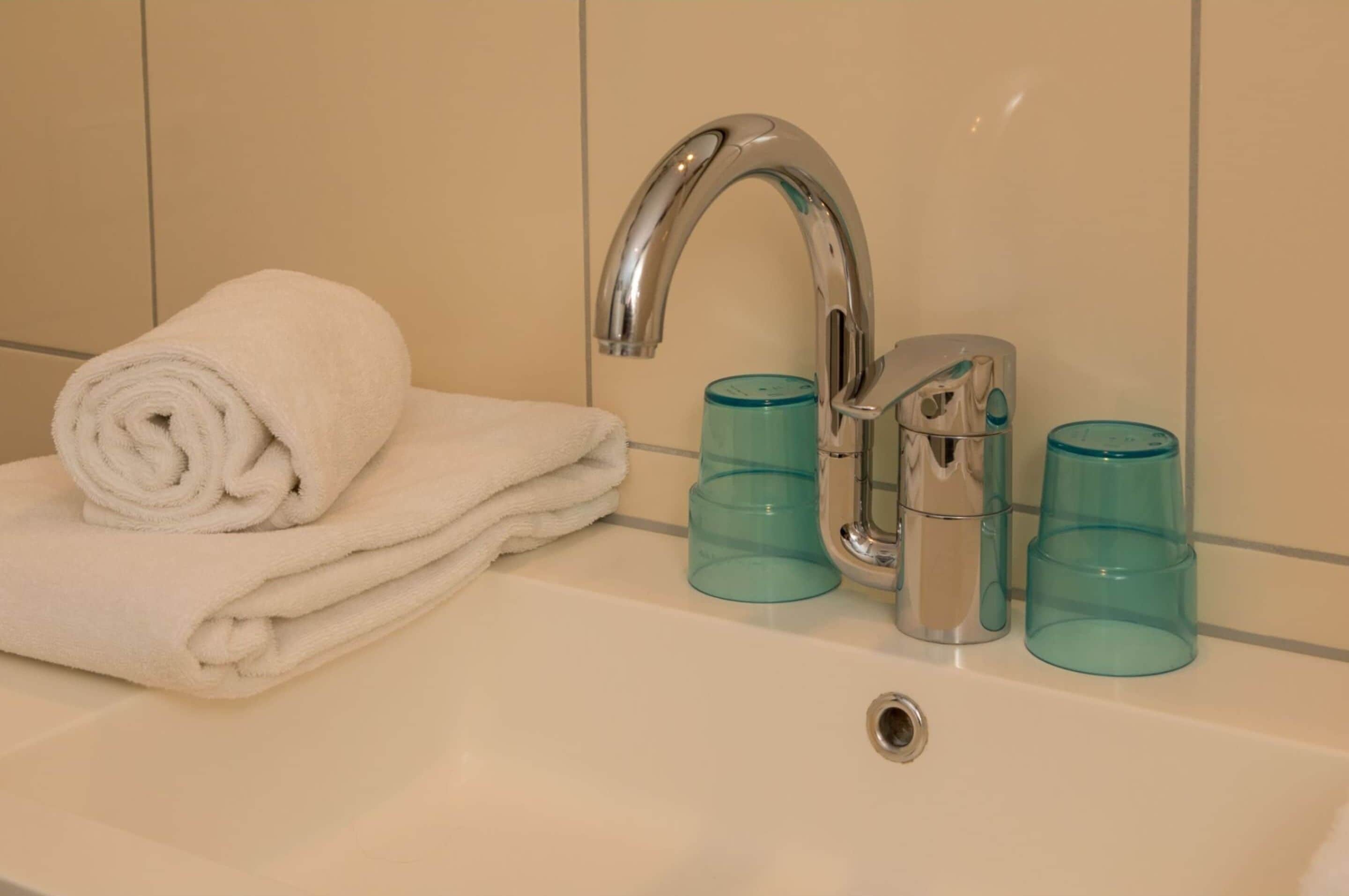 A bathroom with a white sink, a silver faucet, and three blue glass containers.