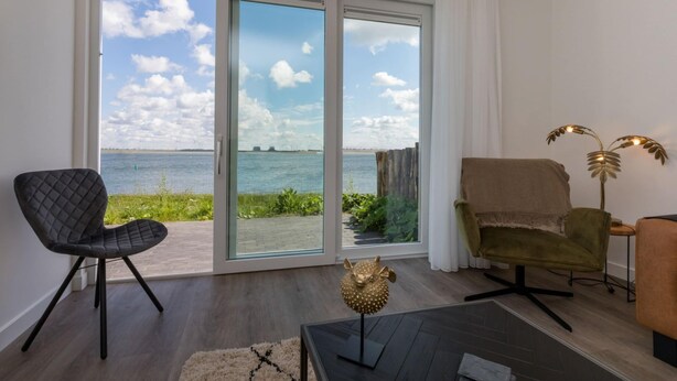 Sala de estar moderna com vista para o mar, apresentando uma poltrona preta, um sofá verde e uma escultura de peixe decorativa sobre uma mesa.