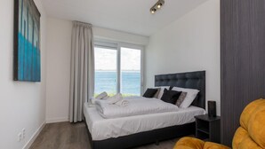 Quarto moderno com uma cama grande, vista para o mar e um quadro na parede.