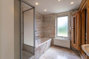 A bathroom with a marble wall, a bathtub, a window, and wooden paneling. - Bungalow Near Oosterschelde Beach (Kamperland)