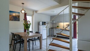 A modern kitchen with white cabinets, a microwave, and a stove. There is a dining area with a wooden table and chairs, and a staircase leading to an upper level. - Bungalow Near Oosterschelde Beach (Kamperland)
