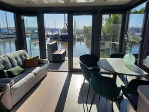 Habitación moderna con sofá, sillas y una mesa, con vistas a un puerto deportivo con barcos.