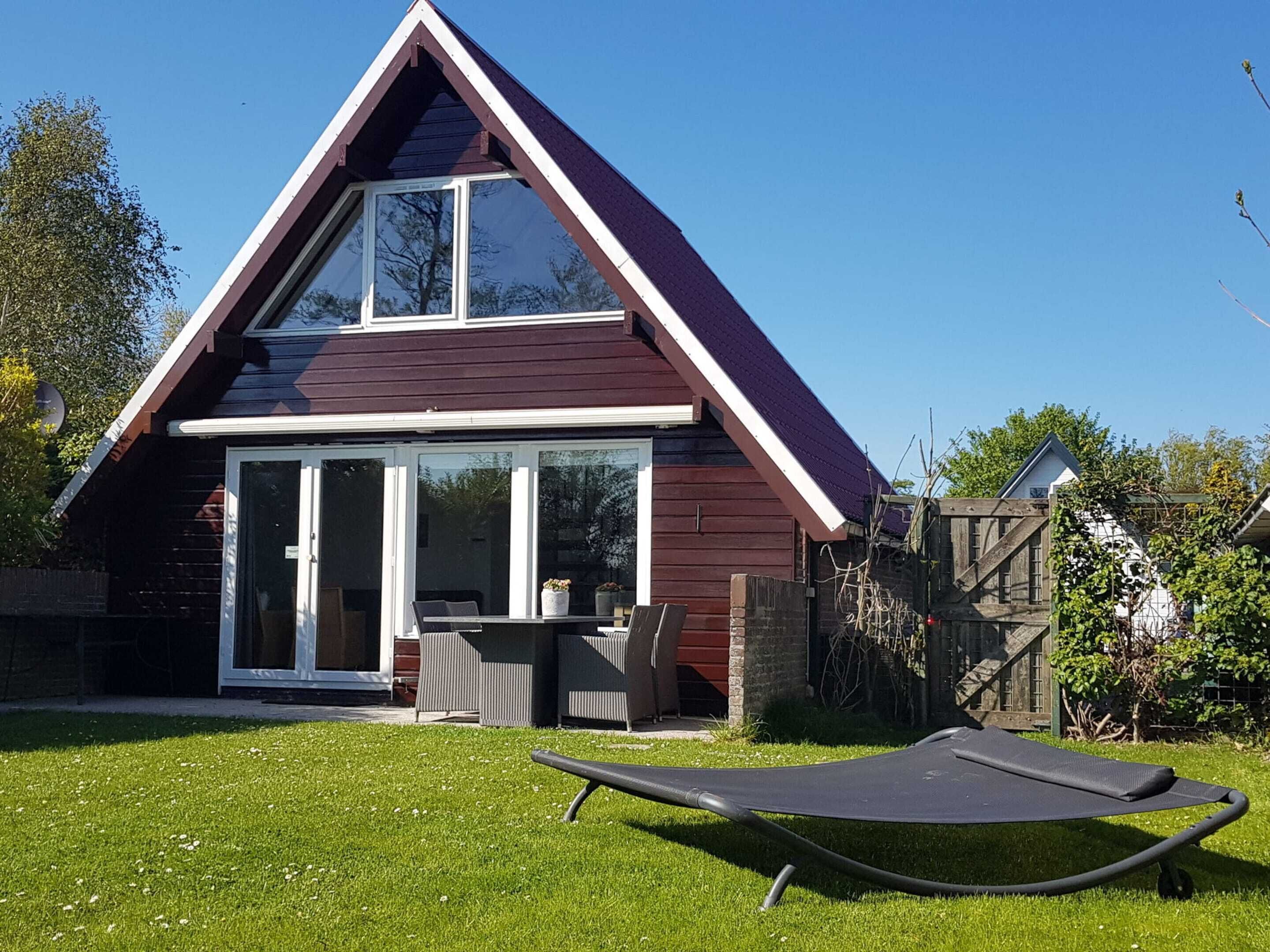 A modern house with a triangular roof, a sliding glass door entrance, and a small patio area with a lounge chair.
