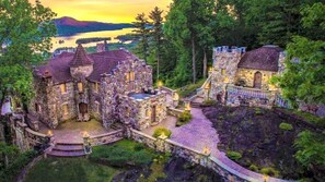 A stone castle with multiple towers and a courtyard, surrounded by lush greenery and a lake in the background.