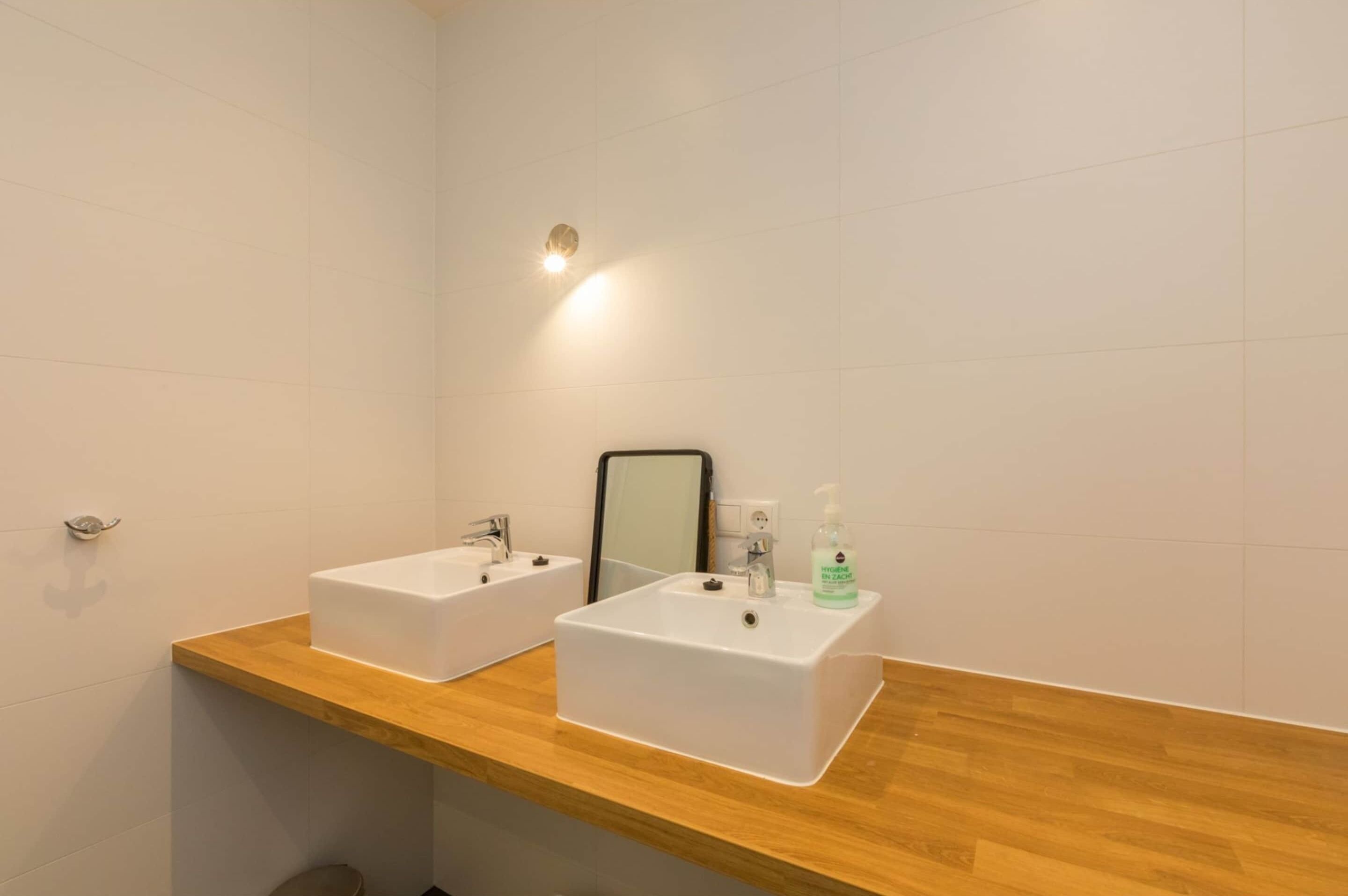 A bathroom with two white sinks, a wooden countertop, a mirror, and a wall-mounted light.
