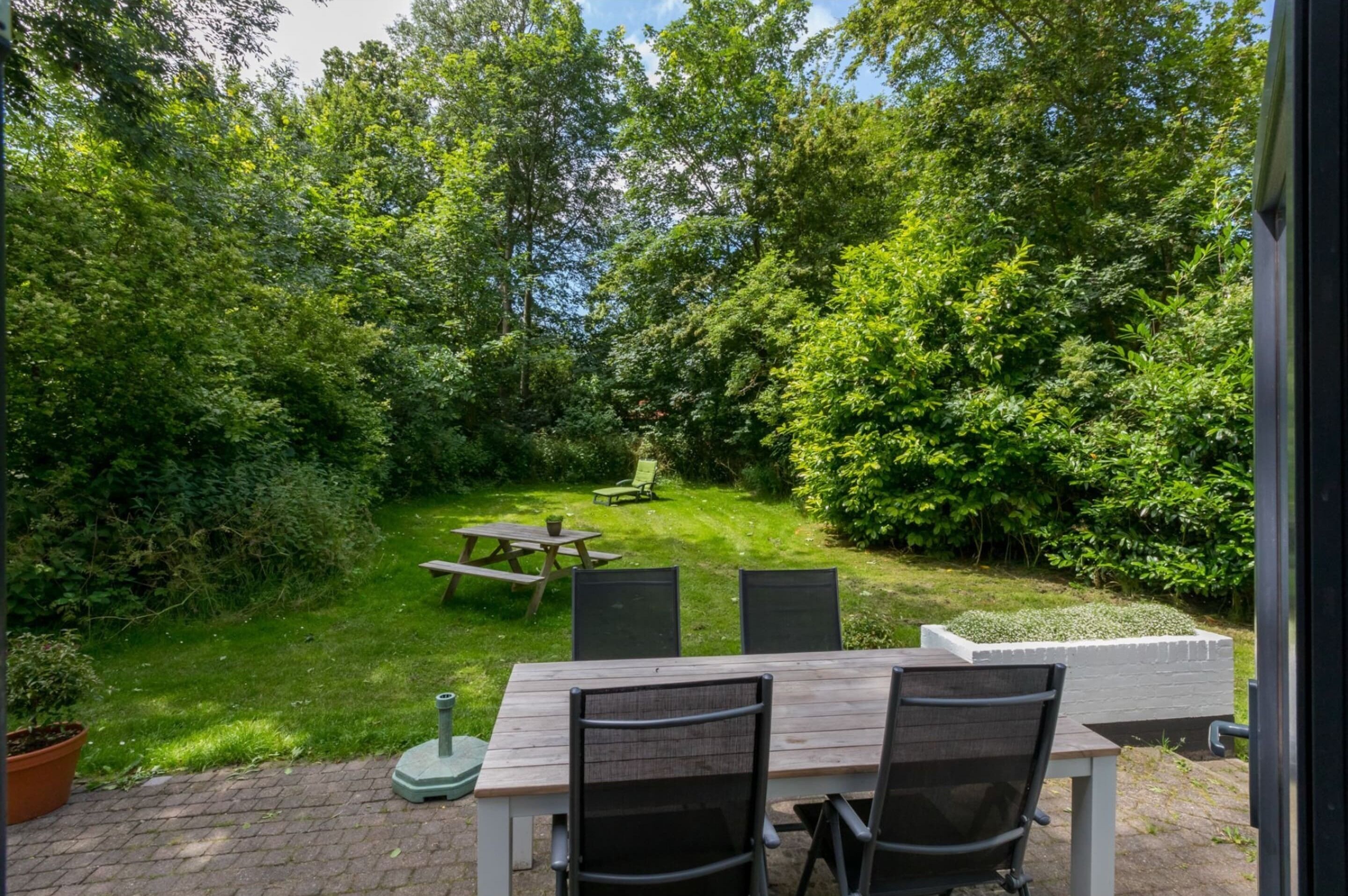 Eine Terrasse im Freien mit Tisch und Stühlen, umgeben von üppiger Vegetation und Bäumen.