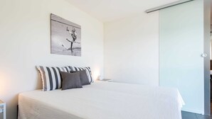 Un dormitorio moderno con una cama grande, almohadas a rayas, un cuadro en la pared y una puerta corredera.