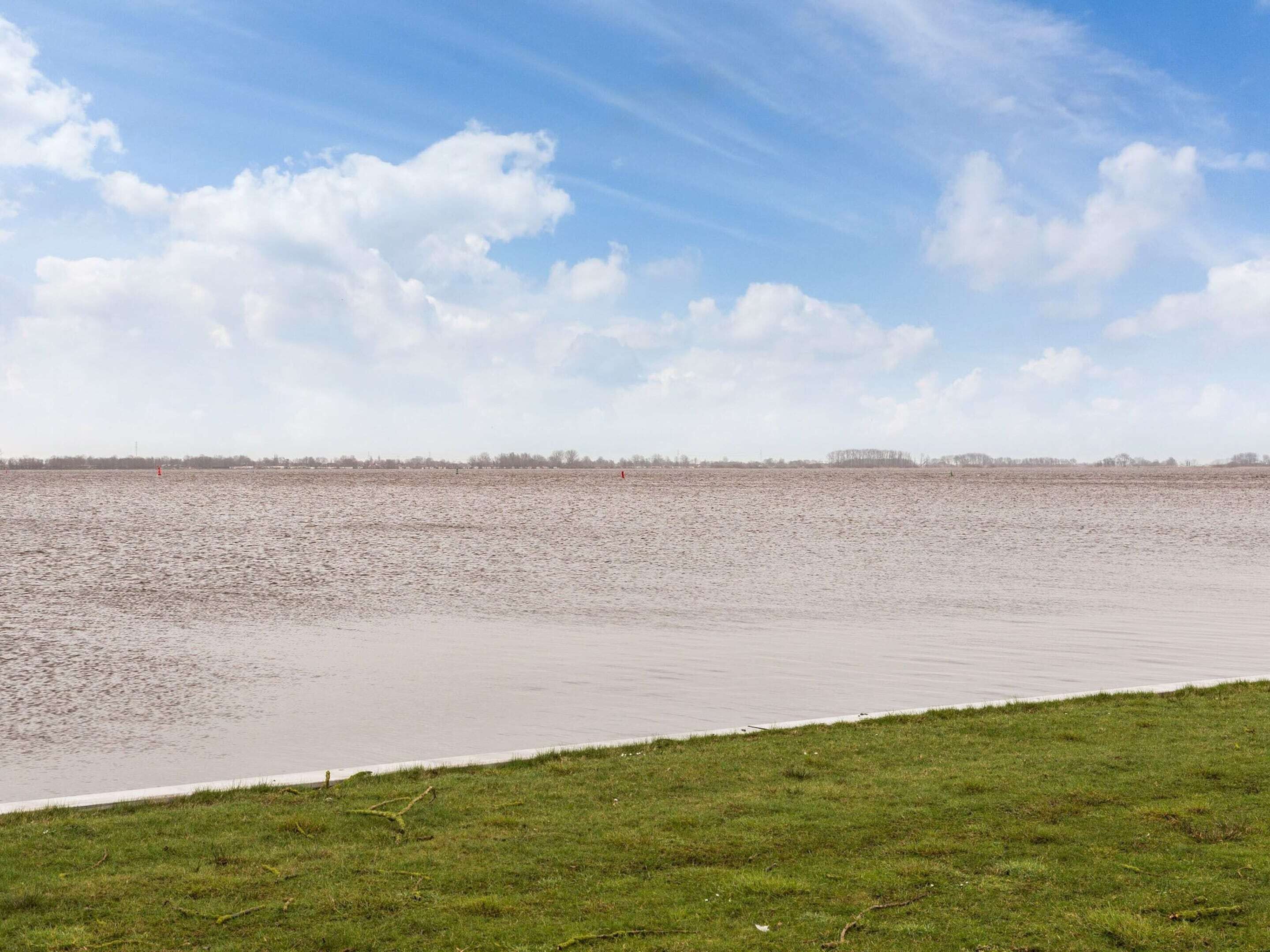 Une large rivière aux rives verdoyantes, sous un ciel dégagé.