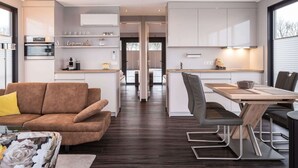 A modern kitchen with white cabinets, a dining area with a wooden table and chairs, and a living room with a brown sofa and a coffee table. - Houseboat With Stunning Views (Offingawier)