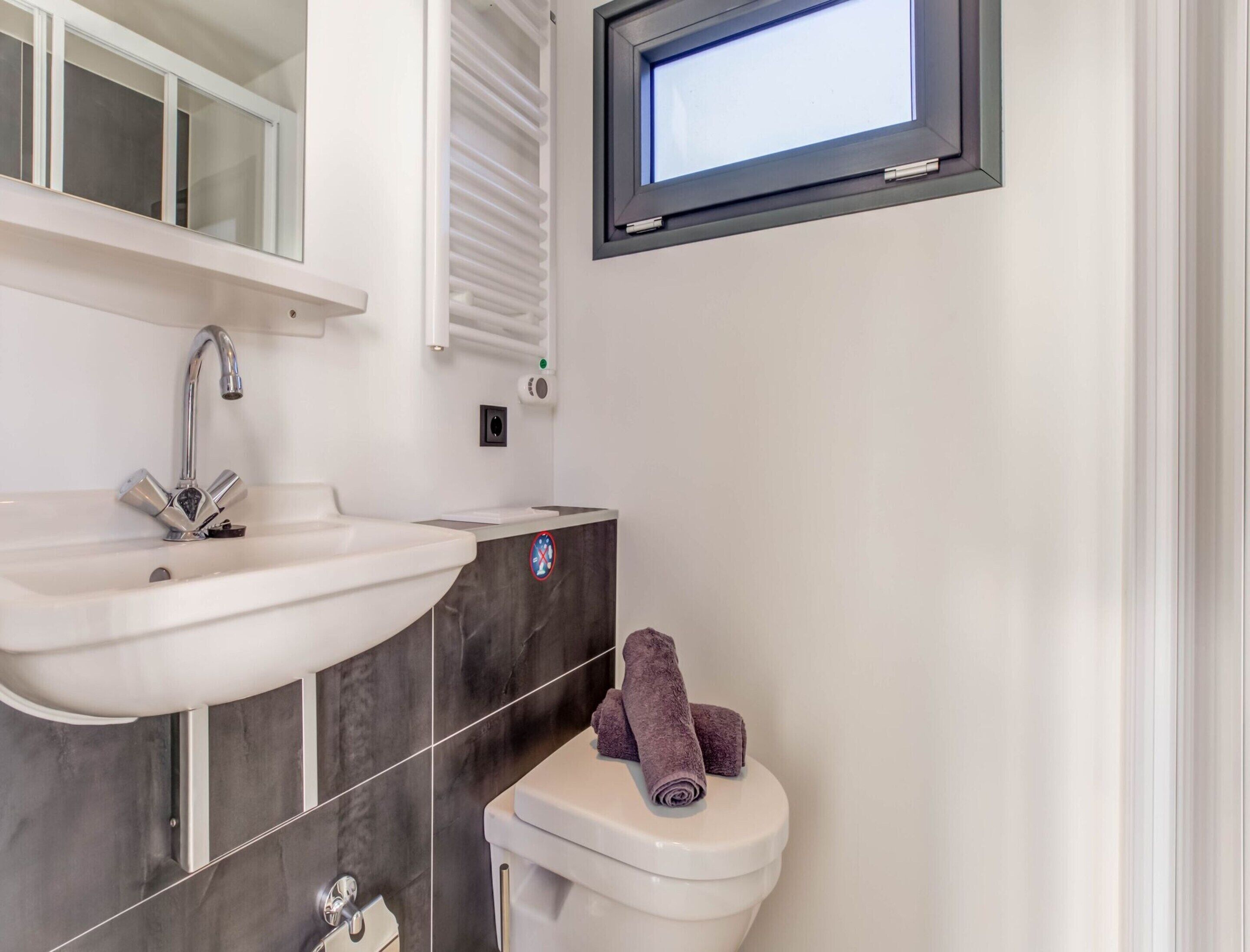 Een badkamer met een wit wastafelmeubel, een spiegel, een toilet en een televisie bovenop het toilet bevestigd.