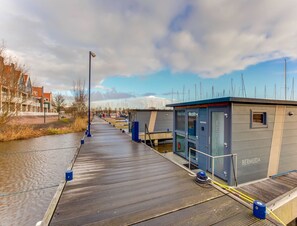 A waterfront promenade with a wooden walkway, a small structure labeled 'BERMUDA', and a row of buildings in the background. - Houseboat in Volendam Near Fort Edam (Volendam)