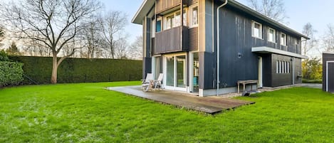 Una casa moderna de dos pisos con un jardín extenso y un porche cubierto.