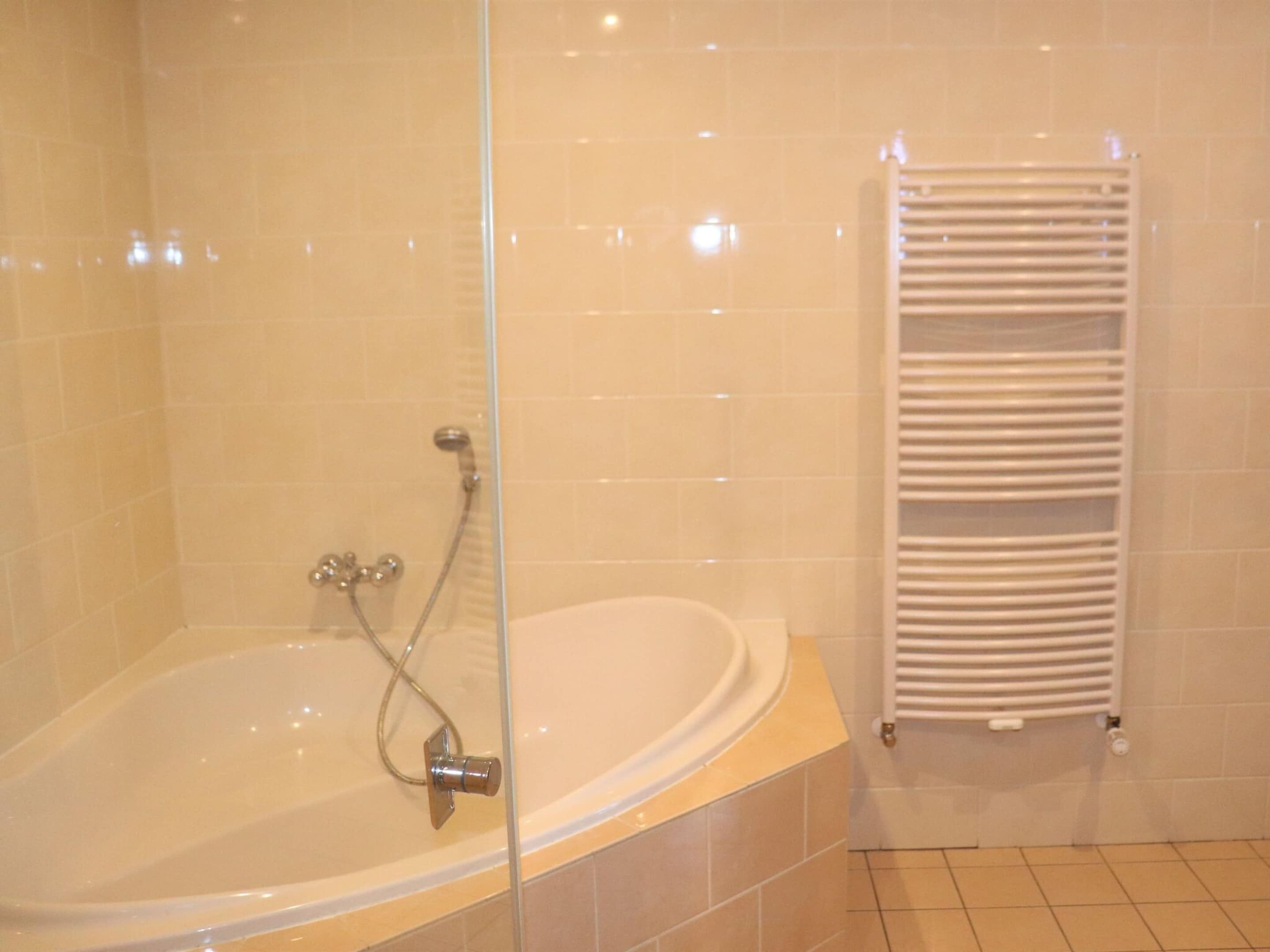A bathroom with a bathtub, a glass shower enclosure, and a white towel rack.