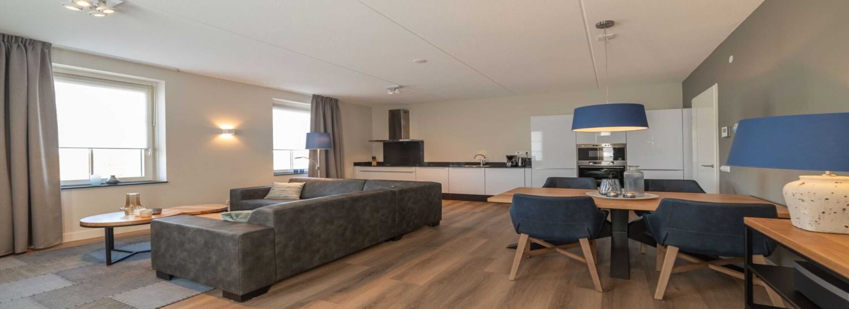 Una habitación de hotel moderna con sofá, mesa de comedor, sillas y zona de cocina.