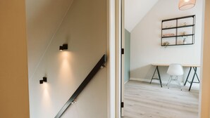Un interior moderno con una escalera de madera, un escritorio con una silla y un estante de pared con objetos decorativos.