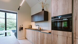 Una cocina moderna con armarios de madera, un horno negro y una ventana con vistas a la vegetación.