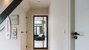 Un pasillo con una puerta que da a una habitación con vistas al exterior. Hay decoraciones en la pared, incluyendo una tabla de surf y un letrero que dice 