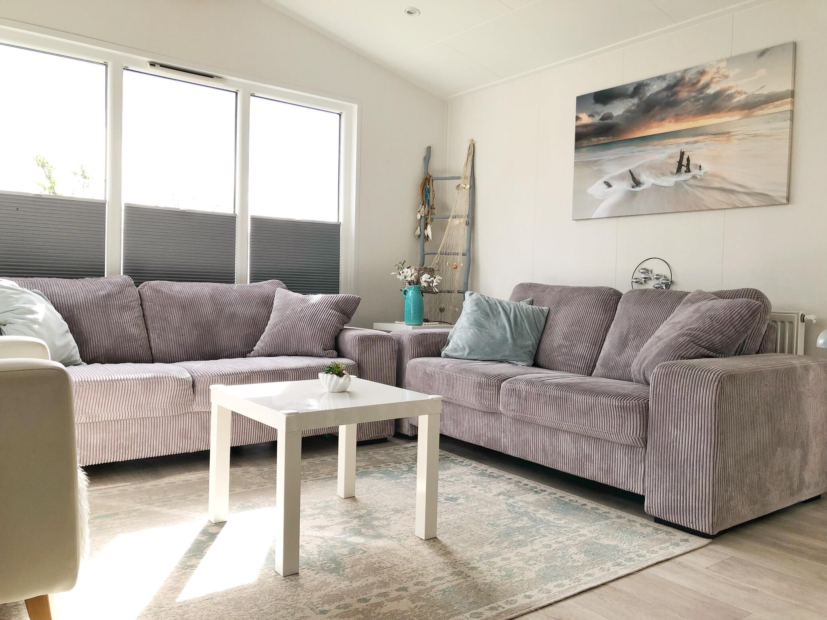A living room with two striped sofas, a white coffee table, and a painting of a beach scene.