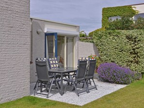 An outdoor patio with a table and four chairs, a door, and a garden with purple flowers. - Modern Furnished Detached Bungalow, Located on the Marina (Kamperland)