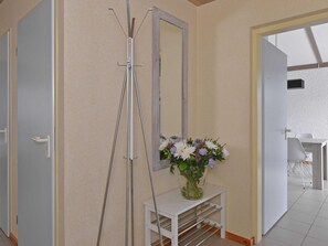 A hallway with a tripod stand, a mirror, and a vase with flowers on a small white table. - Modern Furnished Detached Bungalow, Located on the Marina (Kamperland)
