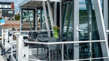 A modern outdoor deck with metal railings, a table with chairs, and a vase with flowers.