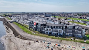 A marina with boats, a beach with people, and a modern building with balconies. - Apartment in Sint-annaland With Water Views (Sint-Annaland)