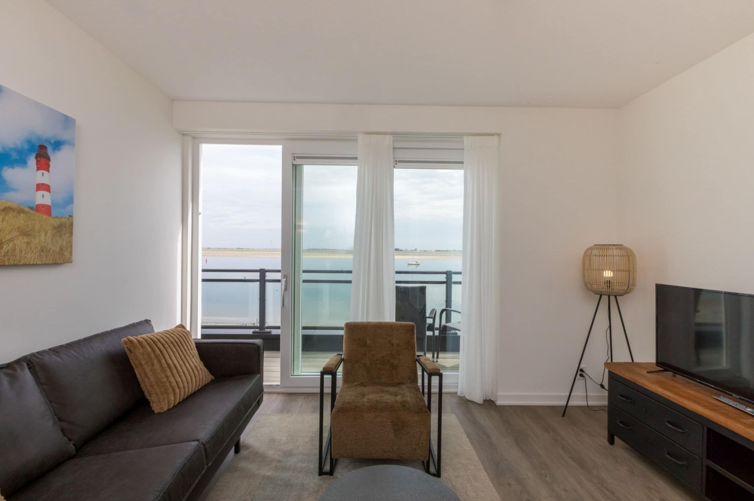 Uma sala de estar moderna com um sofá, poltrona, TV e uma luminária.