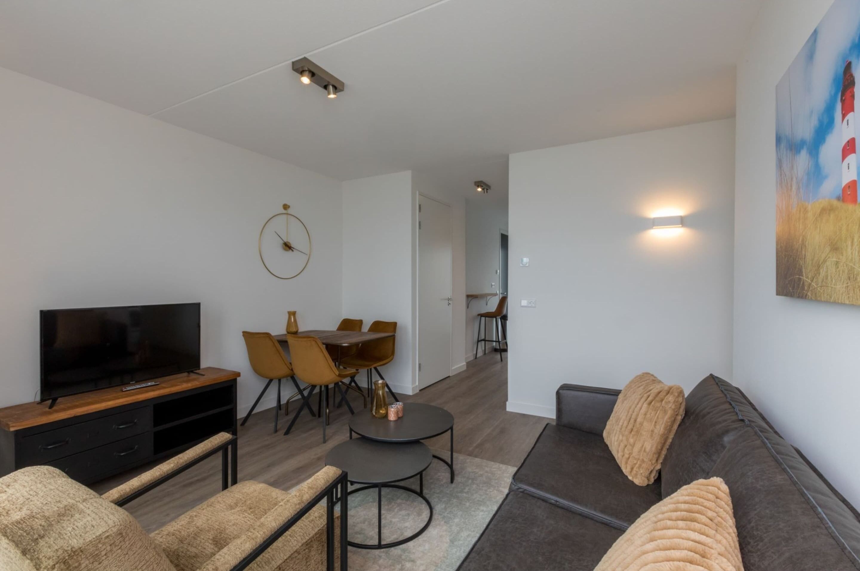 A modern living room with a flat-screen TV, a dining area with chairs, a sofa with cushions, and a painting on the wall.