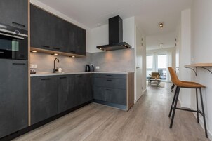 A modern kitchen with dark cabinets, a built-in oven, and a coffee machine.