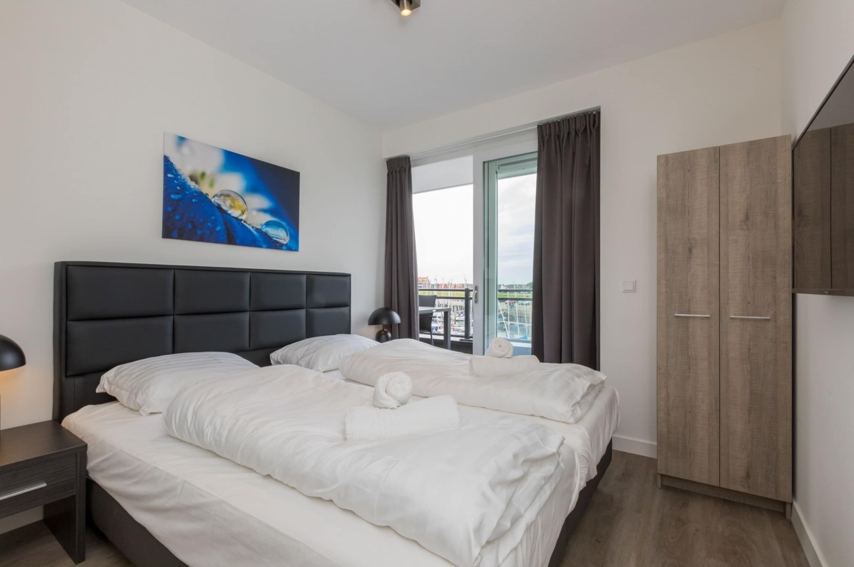 Ein Hotelzimmer mit Bett, Schrank, einem Fenster mit Vorhängen und einem Bild an der Wand.