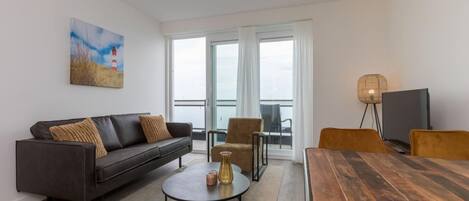 A modern living room with a sofa, coffee table, dining table, and a painting on the wall.