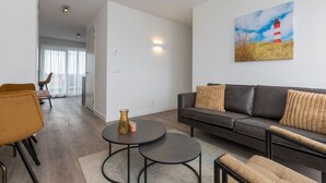 A modern living room with a sofa, two round tables, and a painting of a lighthouse. - Apartment in Sint-annaland With Water Views (Sint-Annaland)