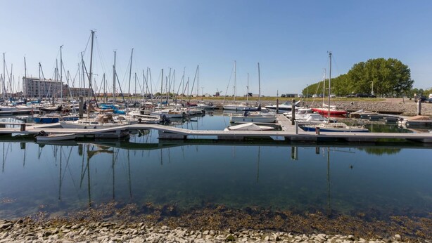 Un port de plaisance où sont amarrés de nombreux bateaux, avec une eau claire et une côte rocheuse.