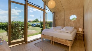 Un dormitorio con cama de madera, ventana circular y vistas a un jardín y vehículos estacionados.