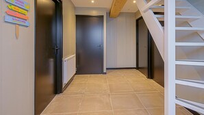 A hallway with a tiled floor, a wooden staircase, and a door with a radiator. - Attractive Holiday Home in Callantsoog With Fenced Garden (Callantsoog)