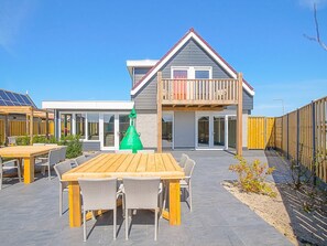 A modern house with a balcony, a wooden deck, and a patio with a table and chairs.