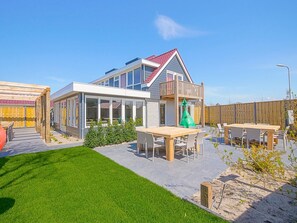 A modern house with a balcony, a patio with a table and chairs, and a well-maintained lawn. - Attractive Holiday Home in Callantsoog With Fenced Garden (Callantsoog)