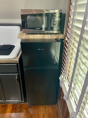 A compact kitchen with a microwave on top of a refrigerator, a sink, and a window with blinds.