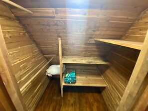 Une petite pièce en bois, avec un plafond en pente, une étagère en métal et un banc en bois.