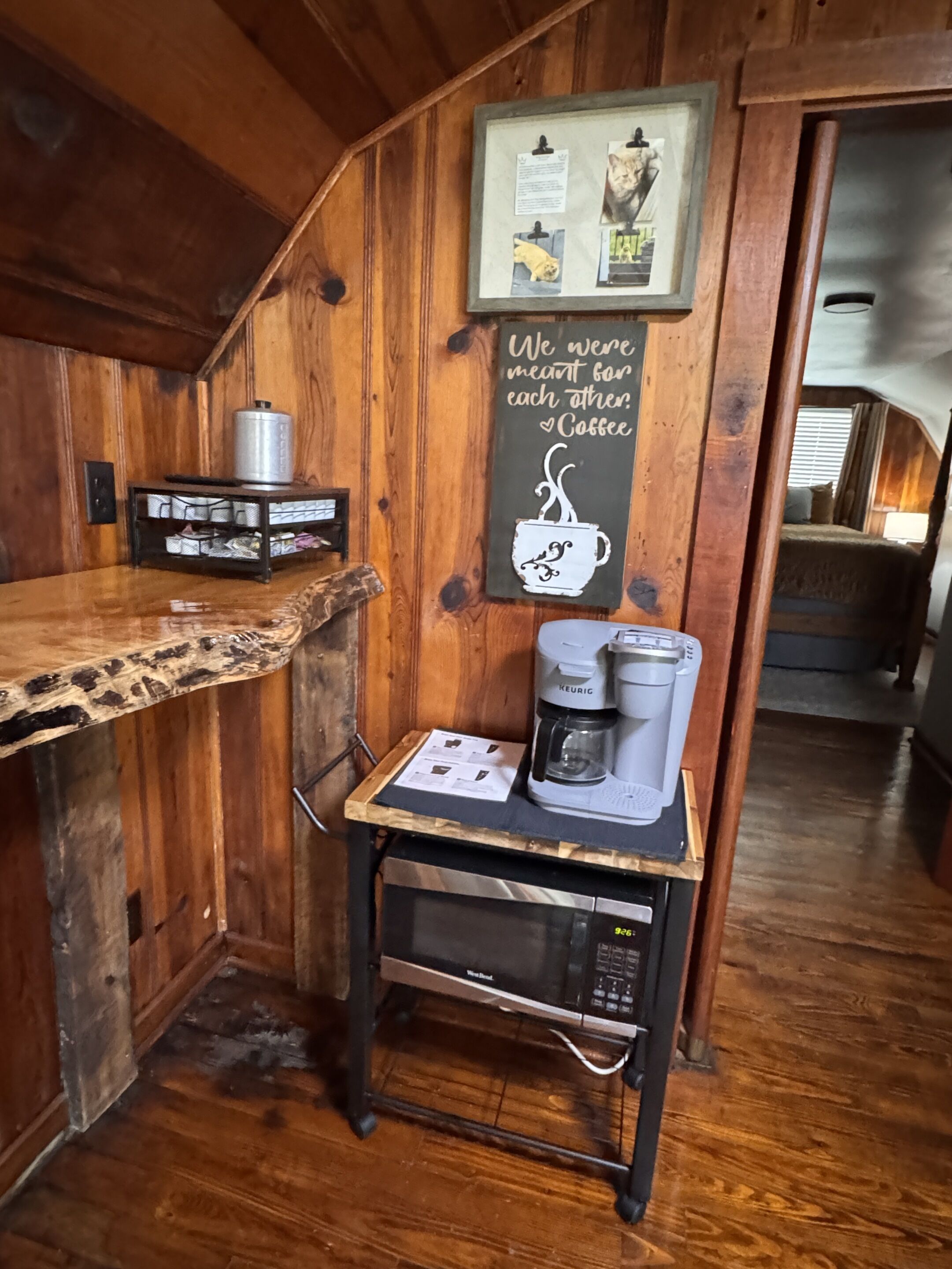 A wooden interior with a coffee station featuring a Keurig machine, a framed picture with cats, and a sign with a coffee cup.