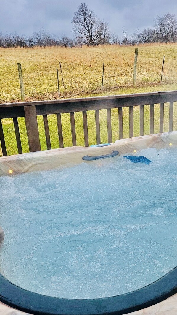 Un bain à remous dans un jardin, avec une clôture en bois et un champ verdoyant en arrière-plan.