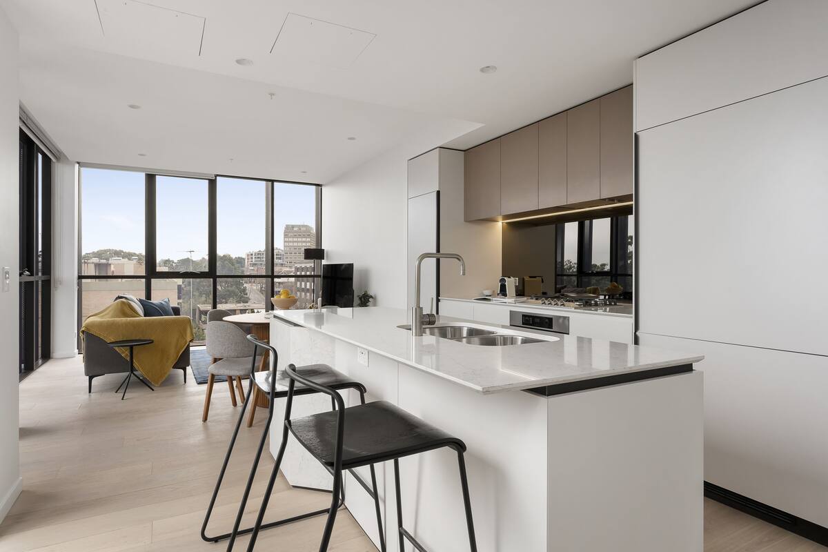 A modern kitchen with a large island, bar stools, and a view of the city through large windows.
