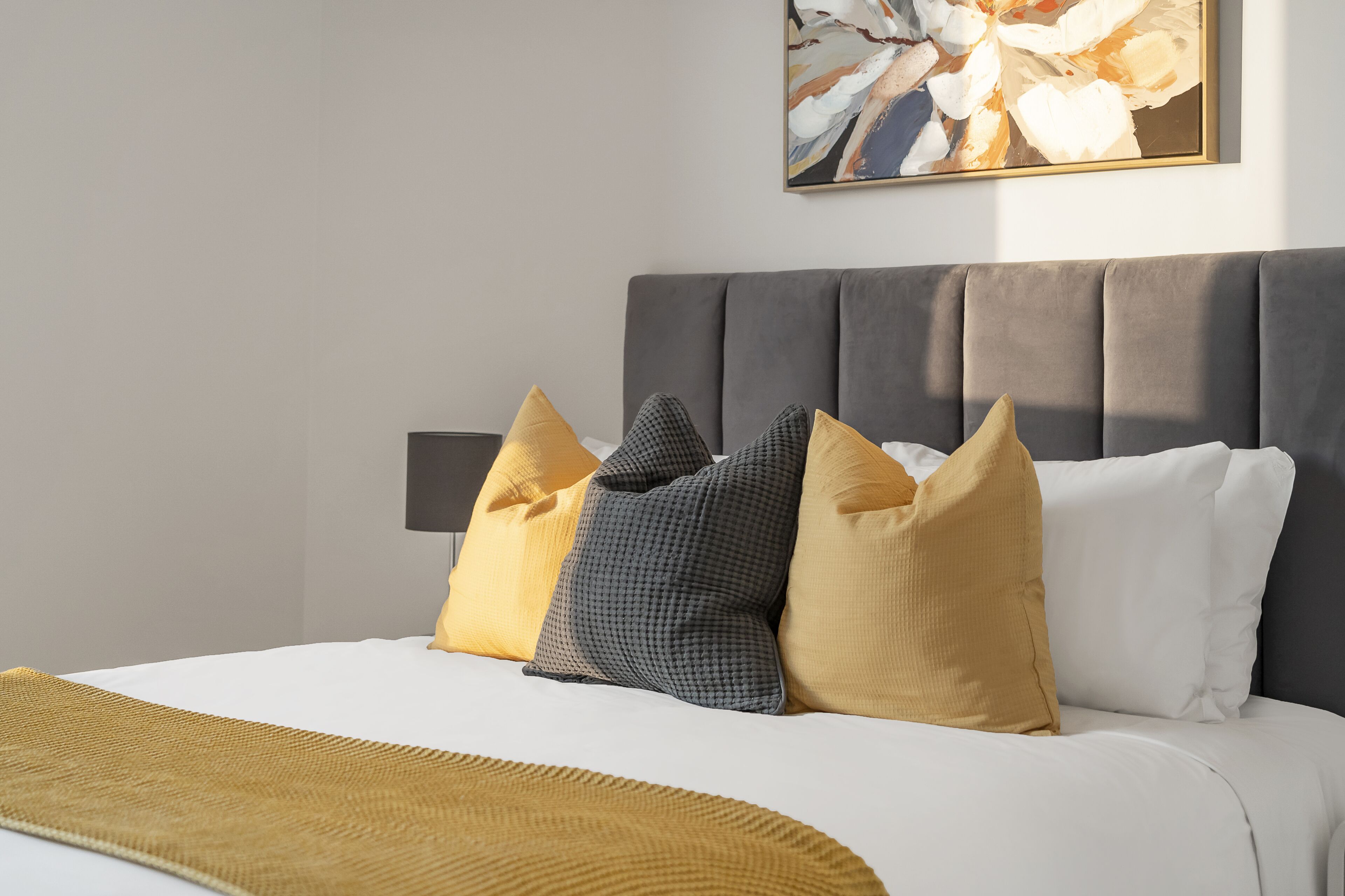 A neatly made bed with a gray headboard, white and mustard-colored pillows, and a mustard-colored throw blanket.