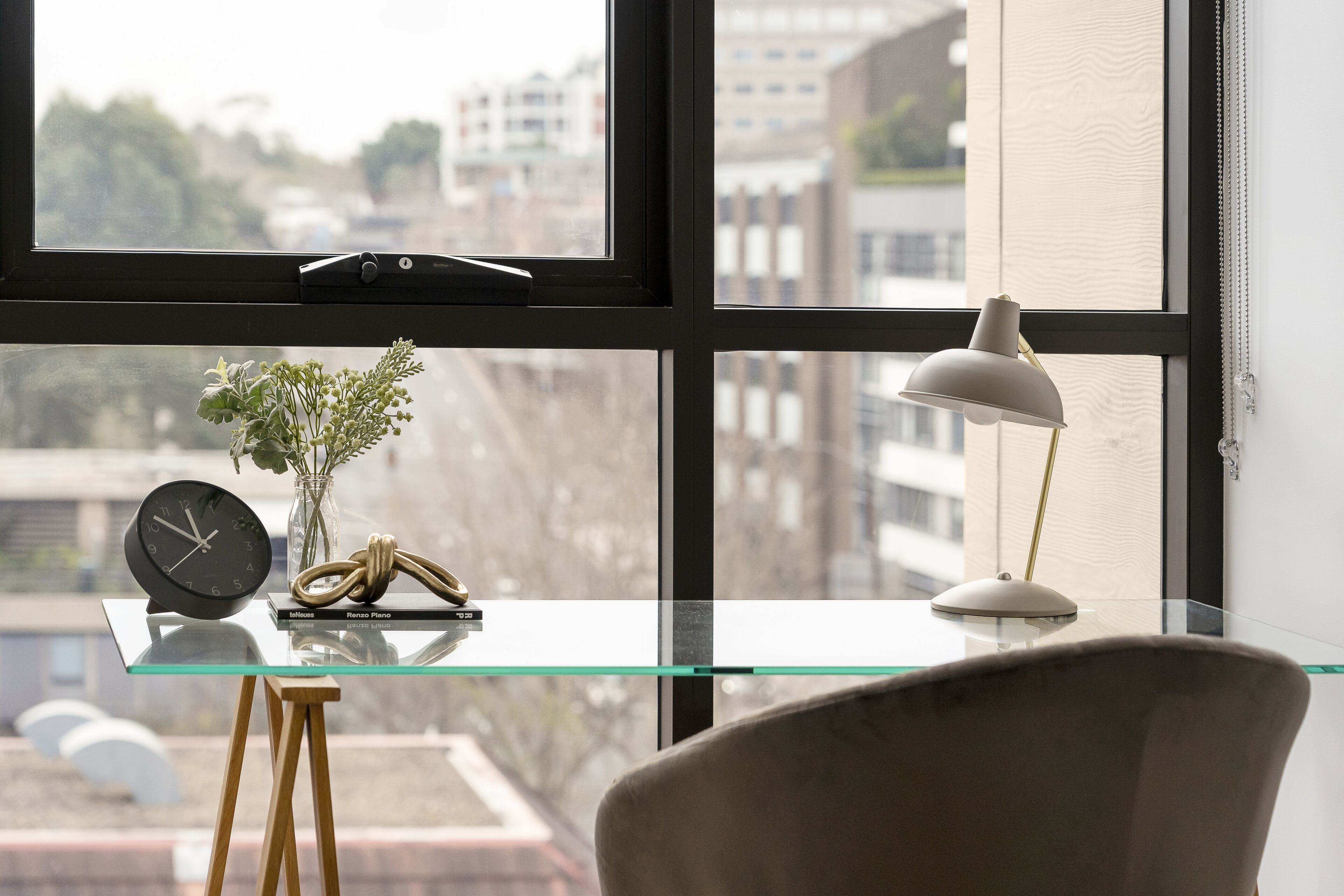 Une pièce moderne avec une table en verre, une horloge, une lampe et une chaise.