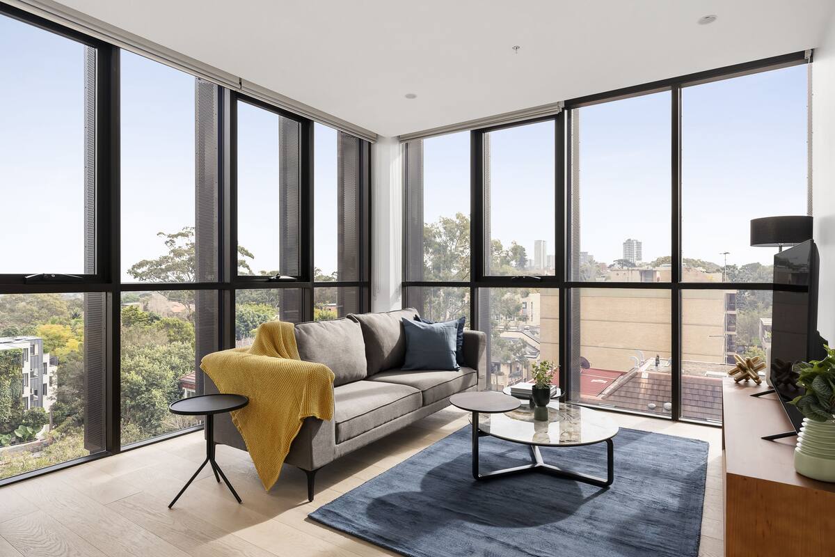 A modern living room with a sofa, coffee table, and a view of the city through large windows.